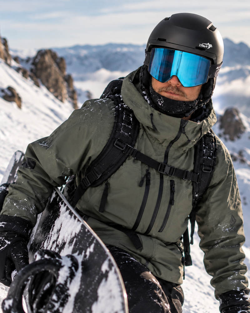 Casco sci e snowboard DMN NIVAL nero opaco con ventilazione integrata, indossato da uomo con maschera blu sulle montagne innevate.
 Copia ALT